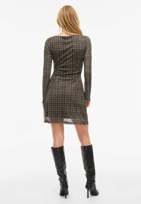 Robe à manches longues en tartan aux tonalités sombres, avec une taille cintrée et une longueur au genou. Accompagnée de bottes noires hautes au fini élégant.