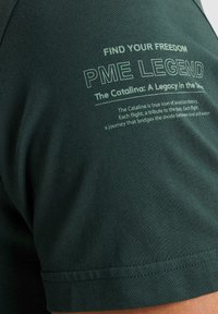 Zelena majica s natpisom "PRONAĐI SVOJU SLOBODU PME LEGEND" i detaljima o Catalina. Mekani materijal s glatkom teksturom.
