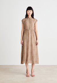 Rjava obleka do kolen s kratkimi rokavi, zategnjenim pasom in herringbone teksturo. Kombinirana s nude, trakastimi petami na nevtralni podlagi.