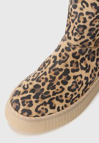 Leoprint Wildleder-Stiefelette mit runder Spitze, flexibler Gummisohle und geflochtenem Rand entlang der Kante. Weiche Textur mit schwarzen Flecken.