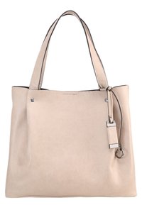 Sac cabas en cuir beige avec deux poignées, rivets métalliques et petite étiquette en cuir attachée avec détail anneau métallique.