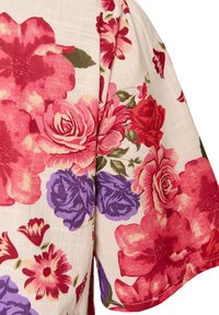 Ύφασμα με κόκκινο, ροζ και μοβ floral σχέδιο σε ανοιχτό μπεζ φόντο, εστιάζοντας σε τμήμα μανικιού με ορατές λεπτομέρειες λουλουδιών.