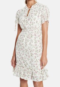 Blommig mini-klänning i ett ljust krämfärgat tyg, med rosa blommor, korta ärmar med knytdetaljer, resårmidja och volangslut.