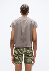 Κοντομάνικο γκρι πουκάμισο με υφή υφάσματος και ορατές ραφές, σε συνδυασμό με πράσινα σορτς καμουφλάζ με εφαρμοστή σχεδίαση.