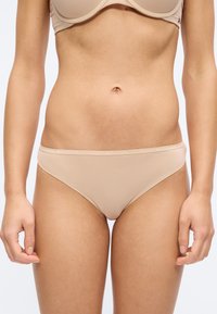 Γυναίκα με σουτιέν Tommy Hilfiger σε γυμνό χρώμα και ταιριαστό εσώρουχο τύπου μπικίνι, εμφανιζόμενη από τη μέση μέχρι το πάνω μέρος των μηρών.