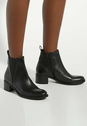 Black ankle boots made of textured leather with a rounded toe, side zipper, and a low block heel. Features a pull tab at the back.