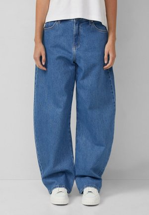 Brede blauwe denim jeans met een hoge taille, voorzien van een klassieke vijf-pocketontwerp en witte sneakers. Glad stofoppervlak, casual stijl.