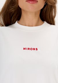 Witte sweatshirt met rode geborduurde tekst "MIRONS" op de borst. De stof lijkt glad met een klassieke ronde halsontwerp.