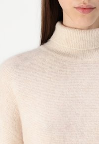 Cremfarbener Rollkragenpullover, gestrickte Textur, weicher Stoff, dezentes Muster, taillierter Schnitt, hoher Kragen, glatte Verarbeitung am Hals.