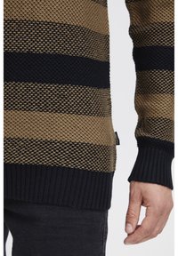 Maglione a maglia con righe orizzontali in marrone chiaro e blu navy, caratterizzato da una trama texturizzata, polsini a coste e un'etichetta con logo sul lato.