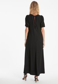Zwarte maxi jurk met puffmouwen, met een keyhole detail op de rug. Gemaakt van zachte stof, heeft het een vloeiende silhouette en een ingetogen ontwerp.