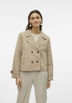 Veste double boutonnage beige avec un col cranté, ornée de grands boutons et de poches latérales, associée à un pantalon texturé gris clair.