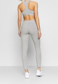 Set di reggiseno sportivo e leggings grigi, realizzati in tessuto elasticizzato. Il reggiseno presenta un design a schiena scoperta, mentre i leggings hanno una vestibilità slim e sono lunghi fino alla caviglia.