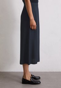 Dunkelblaue Midirock aus leichtem Stoff, fließende Form, dezenter Glanz, kombiniert mit schwarzen Loafers mit goldenen Akzenten.