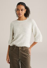 Pulover gri deschis, tricotat cu textură și model de diamante, cu mâneci trei sferturi, combinat cu pantaloni din catifea de culoare verde măsliniu.