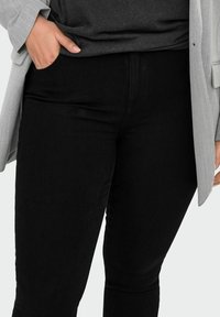 Svart denimjeans med slim fit, med hög midja och lätt stretch. Matchas med en grå långärmad topp och blazer.