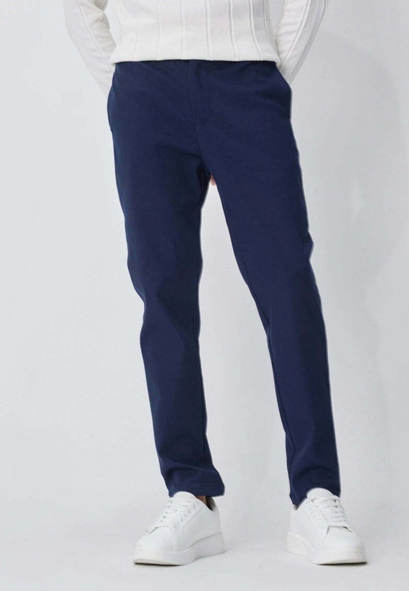 Personne portant un pantalon slim fit bleu marine et des baskets blanches, avec un pull rayé blanc visible à la taille.