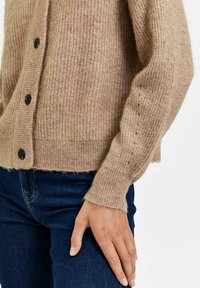 Cardigan beige lavorato a maglia con bottoni neri, texture a coste e vestibilità casual. Presenta maniche lunghe e orlo leggermente accorciato.