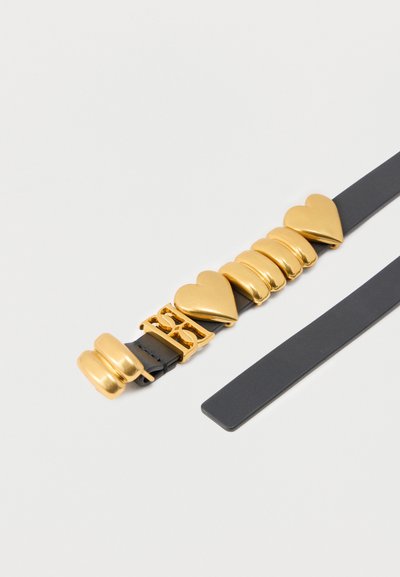 Μαύρη δερμάτινη ζώνη με διακοσμητική λαμπερή χρυσή καρδιά και οβάλ γοητεύει κατά μήκος μιας πλευράς.