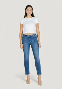 Valkoinen lyhennetty t-paita, jossa kimaltava logo, yhdistetty istuviin keskiharmaisiin farkkuihin. Sileä kangas ja klassinen viiden taskun malli. Korkokengät täydentävät asun.