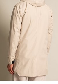 Beige vattentät jacka med huva, med en slät textur, långa ärmar, knappar vid ärmsluten och en rak passform.