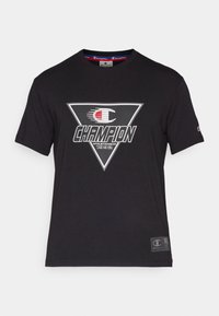 Musta puuvillapaita, jossa on suuri kolmiomainen graafinen kuvasto, jossa lukee "CHAMPION", punaiset ja valkoiset yksityiskohdat sekä pieni logo hihassa.