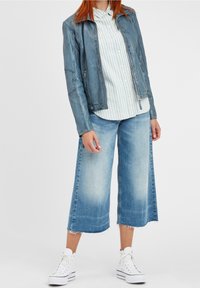 Giacca di pelle blu chiaro, camicia bianca a righe con bottoni, culotte di denim larghe e sneakers alte bianche. Texture liscia e design informale.