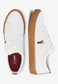 Zapatillas blancas de cuero con suelas de goma, que presentan acentos marrones, un logo bordado y un diseño clásico de cordones.