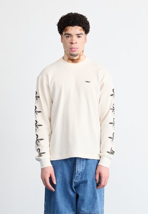 Crème-kleurig, wafelgebreid T-shirt met lange mouwen en zwarte grafische ontwerpen op beide mouwen; heeft een ronde halslijn en een relaxte pasvorm.
