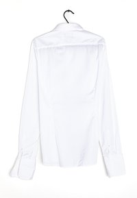 Camisa blanca de manga larga colgada de un gancho negro, con cuello de botón y puños con botón, y una textura de tela lisa y uniforme.