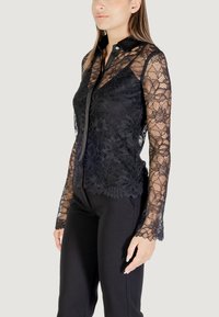 Blusa in pizzo nero con maniche lunghe e trasparenti e colletto nero in contrasto. Presenta intricate fantasie floreali e un design aderente.
