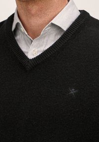 Pull noir à col en V en matière douce, avec un col côtelé. Un logo discret est brodé en fil sombre sur la poitrine.