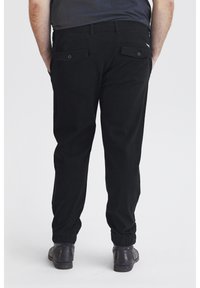 Pantalons en coton noirs avec une coupe décontractée, dotés de poignets élastiques et de deux poches arrière, des détails de couture visibles et une texture lisse.