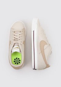Zapatillas beige con un upper de cuero suave, detalles cosidos y un swoosh de Nike en marrón. Plantilla verde con un diseño floral negro.