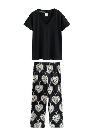 Zwarte top met korte mouwen en V-hals, gecombineerd met een zwarte broek met een wit bloemig hartmedaillonpatroon en een elastische tailleband.