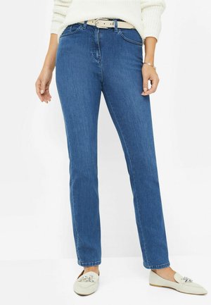 Blauwe denim jeans met een rechte pijp, hoge taille, subtiele stiksels en een beige riem. Gecombineerd met lichtgekleurde, platte instapschoenen.