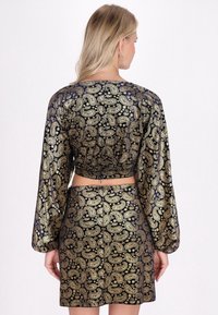 Czarny i złoty top w stylu paisley z długimi rękawami i dopasowaną spódnicą, o gładkiej teksturze i dopasowanej sylwetce.