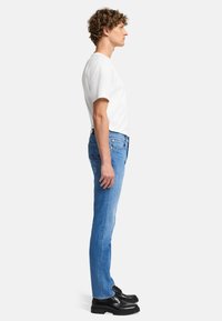 Jasnoniebieskie dżinsy o slim fit, z pięcioma kieszeniami i subtelnymi detalami przeszyć, połączone z białą koszulą na krótki rękaw i czarnymi butami.