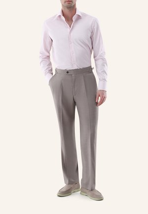 Mann trägt hellrosa kariertes Hemd, taupefarbene hochgeschnittene plissierte Hose und taupefarbene Slipper mit hellen Sohlen.