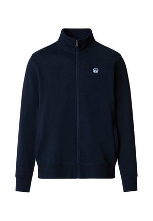 Veste bleu marine à fermeture éclair intégrale avec col montant, poignets et ourlet côtelés, et petit logo de boussole ronde sur la poitrine gauche.