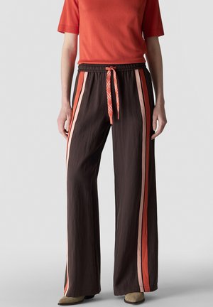 Person wears dark wide-leg pants with vertical red and pink stripes and a red drawstring, paired with a short-sleeve red top and tan shoes.