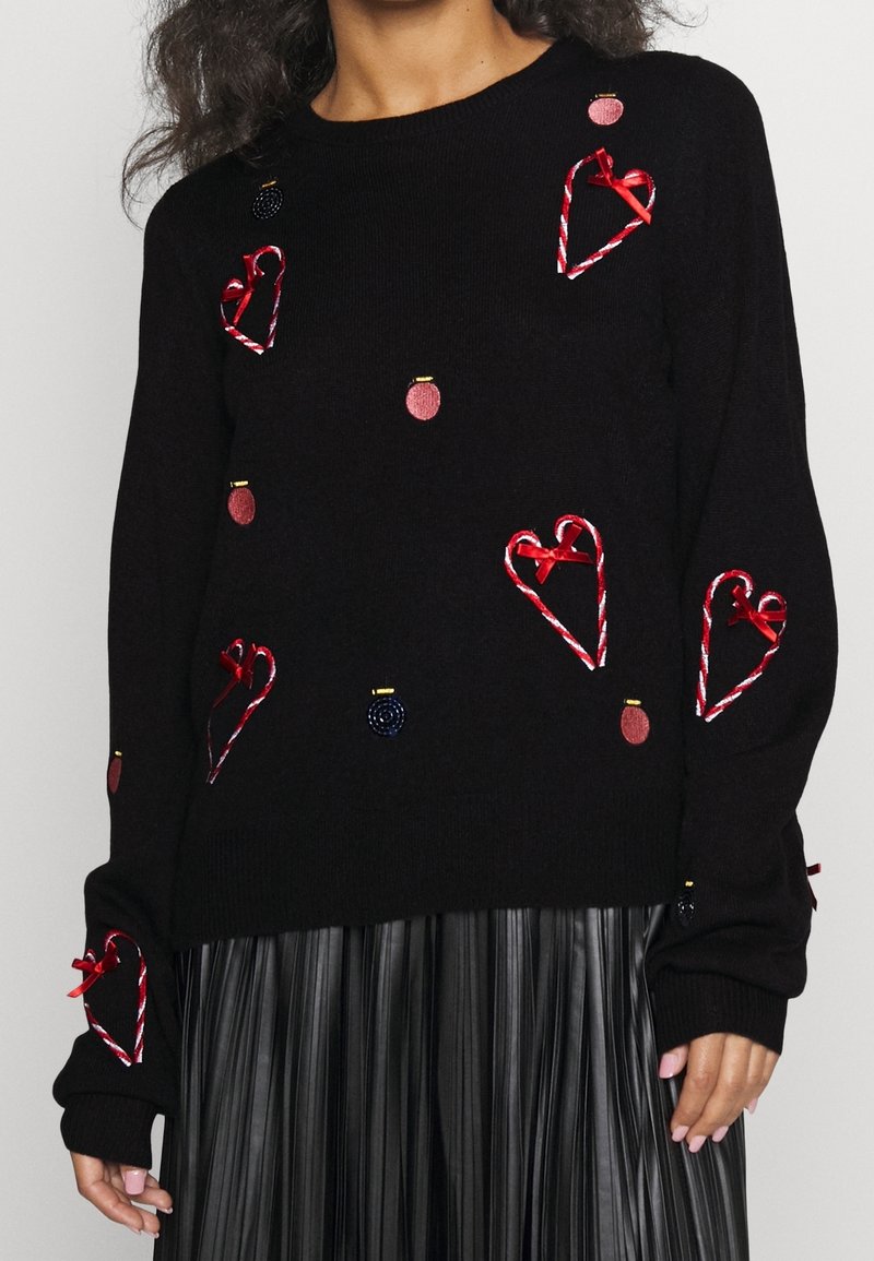 Svart stickad tröja med röda och guld broderade hjärtan och dekorationer, med inslag av pepparkaksgodis och röda rosetter på ärmarna.