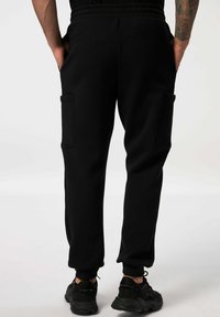 Schwarze Jogginghosen mit einem gerippten, elastischen Bund und seitlichen Aufsatztaschen. Hergestellt aus weichem Stoff mit schmal zulaufenden Beinen und Knöchelbündchen.