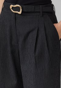 Zwarte pinstripe broek met een gestructureerde afwerking, voorzien van een gouden abstracte riemgesp en voorste plooien. Tailored fit en een slank ontwerp.