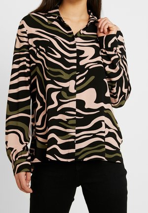 Kvinde iført en skjorte med lange ærmer og knapper med et abstrakt zebra-stribet mønster i sort, lyserød og olivengrøn.