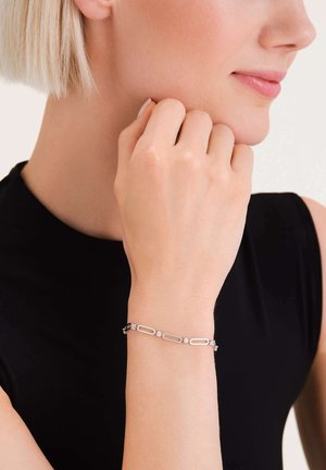 Zilveren armband met ovale schakels en kleine ronde kristallen accenten, gedragen op een blote pols. De achtergrond is neutraal, waardoor de details van de armband beter tot hun recht komen.