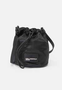 Borsa a secchiello in nylon nero con texture liscia, dotata di un'applicazione del logo e di una tracolla regolabile per opzioni di trasporto versatili.