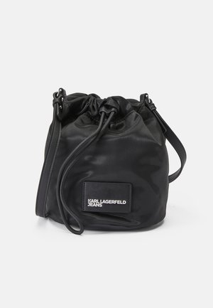 Sac seau en nylon noir avec cordon de serrage, présentant une texture lisse, un patch logo et une sangle réglable pour des options de transport polyvalentes.