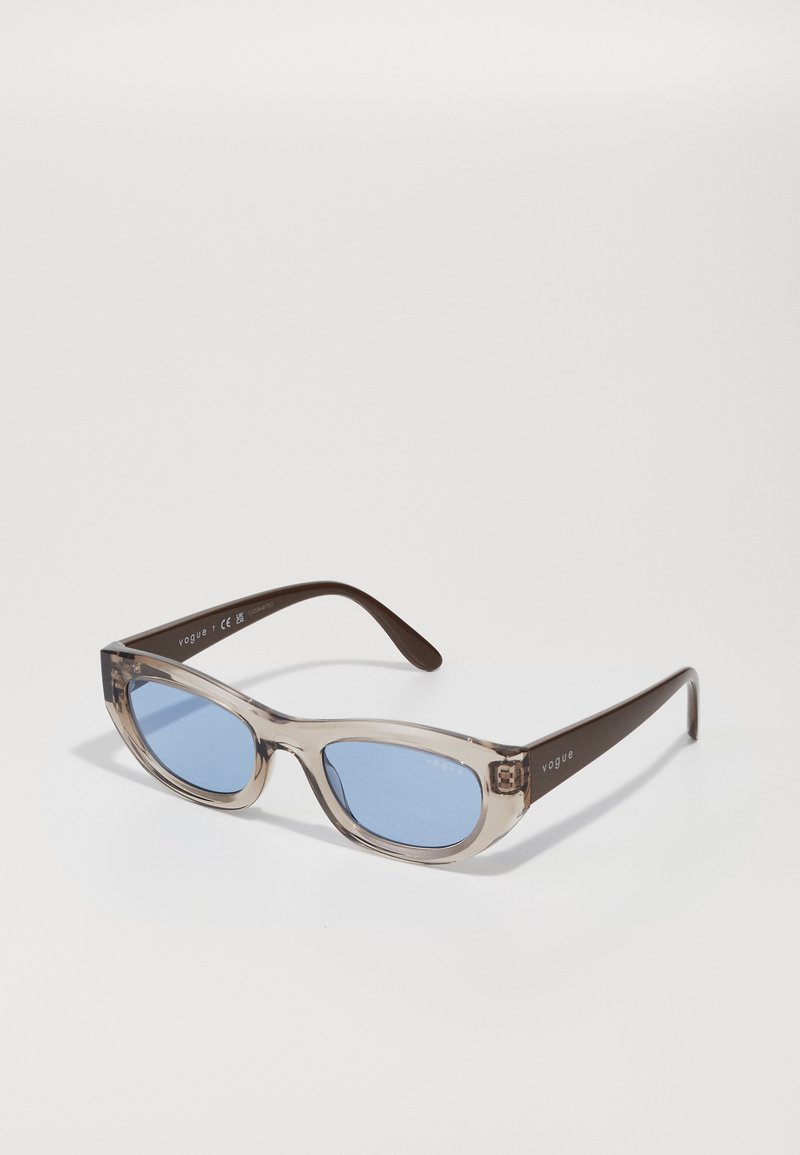 Óculos de sol com armações retangulares transparentes e lentes azuis. Apresenta hastes em castanho com a marca "vogue" em relevo.