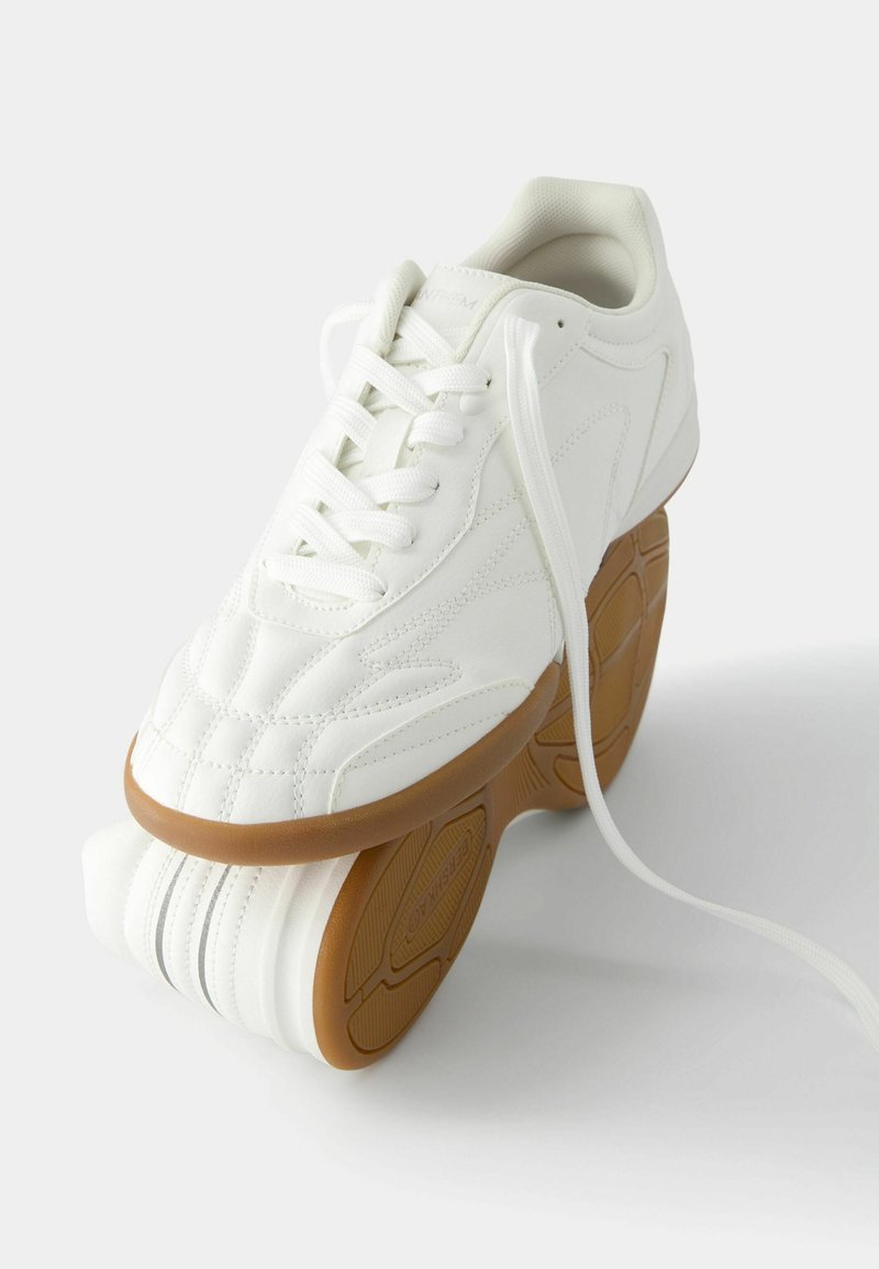 Białe skórzane sneakersy z textured designem, sznurowaniem oraz kontrastującą brązową gumową podeszwą z wzorzystym bieżnikiem.